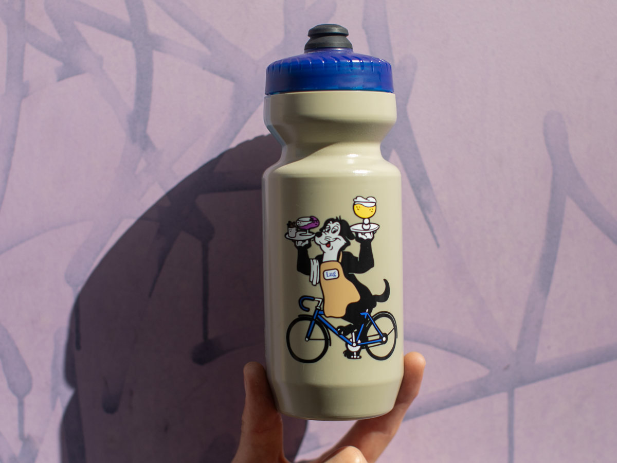 Blue Lug Dog Water Bottle in Mocha — illustration of the Dog mascot in a Lug apron, riding a bike while balancing drinks on serving trays