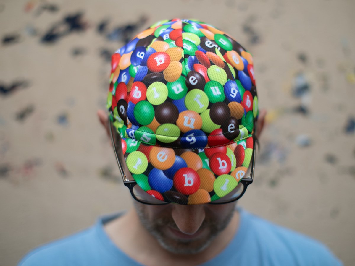 Blue Lug Cycling Cap in Chocolate/Poly, seen from above. The all-over print of colourful candy-coated chocolates with Blue Lug letters covers the entire cap.