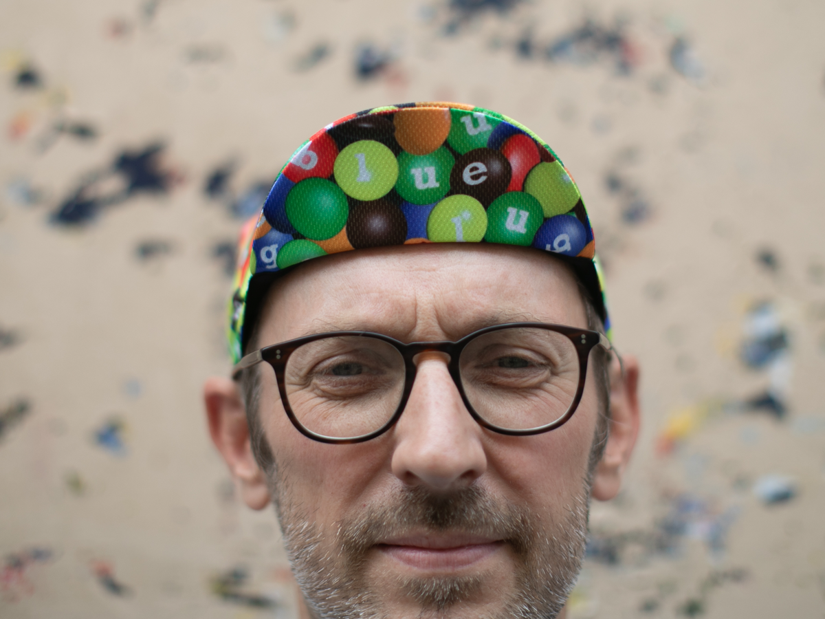 Blue Lug Cycling Cap in Chocolate/Poly worn brim-up. The candy print and Blue Lug lettering are visible across the front panels.