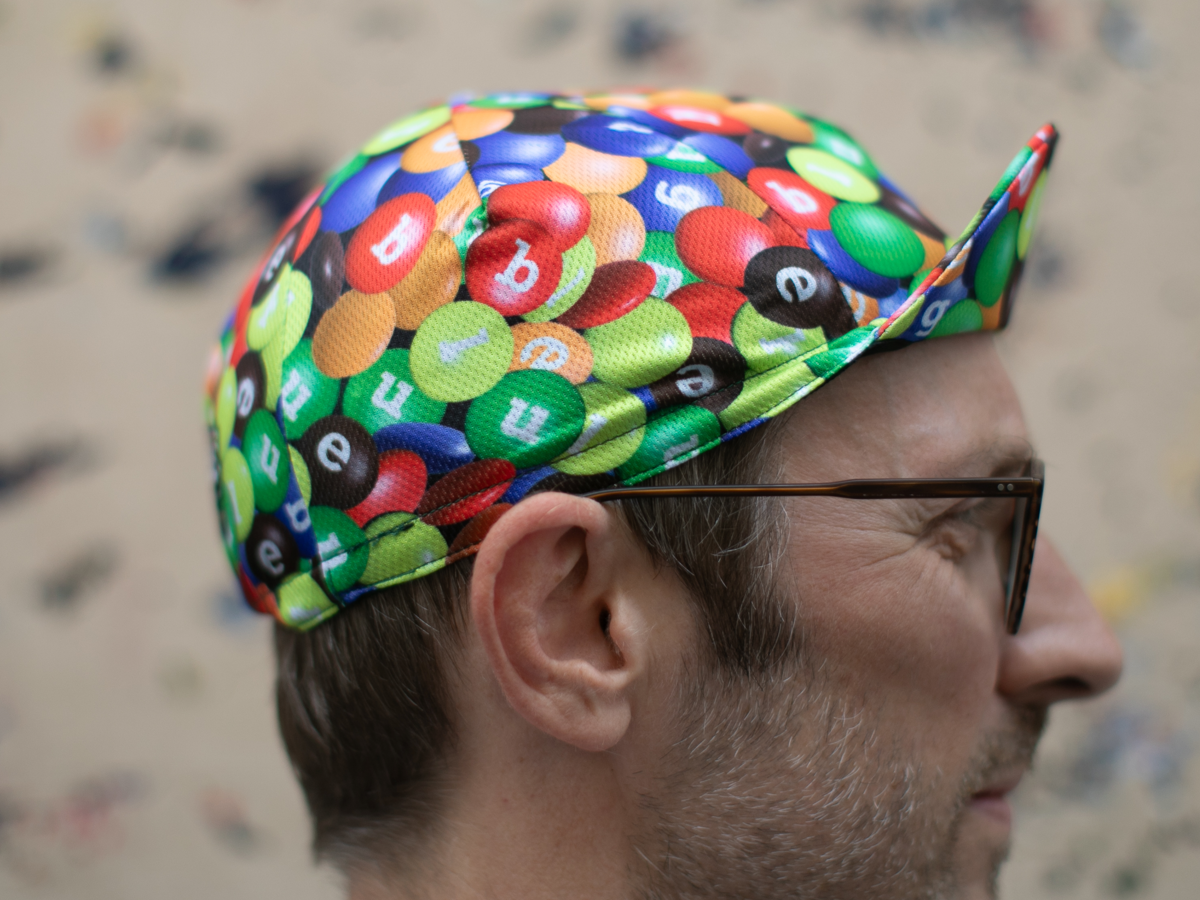 Side view of the Blue Lug Cycling Cap in Chocolate/Poly, showing the classic cycling cap silhouette and the all-over candy-coated chocolate print.