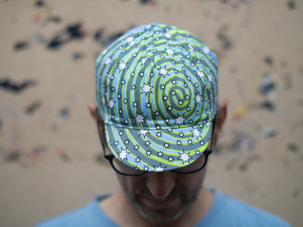Casquette de cyclisme Blue Lug Dreamer, vue de dessus. L'imprimé tourbillon all-over en bleu, gris et jaune-vert fluo avec des étoiles blanches recouvre l'intégralité de la casquette.