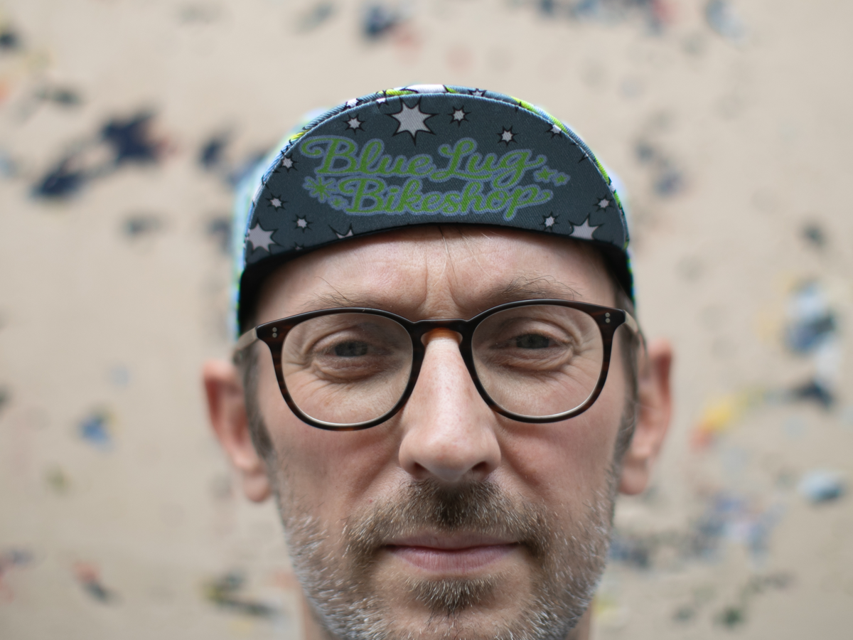 Casquette de cyclisme Blue Lug Dreamer portée visière en avant, vue de face. La visière sombre affiche "Blue Lug Bikeshop" en écriture rétro verte sur fond étoilé.