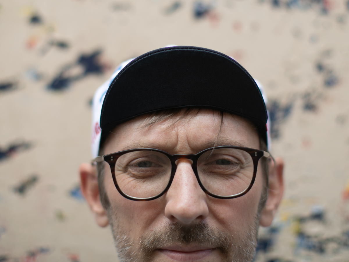 Blue Lug Original Cycle Cap in white worn brim-down, front view. The dark brim contrasts with the white and multicolour panels.