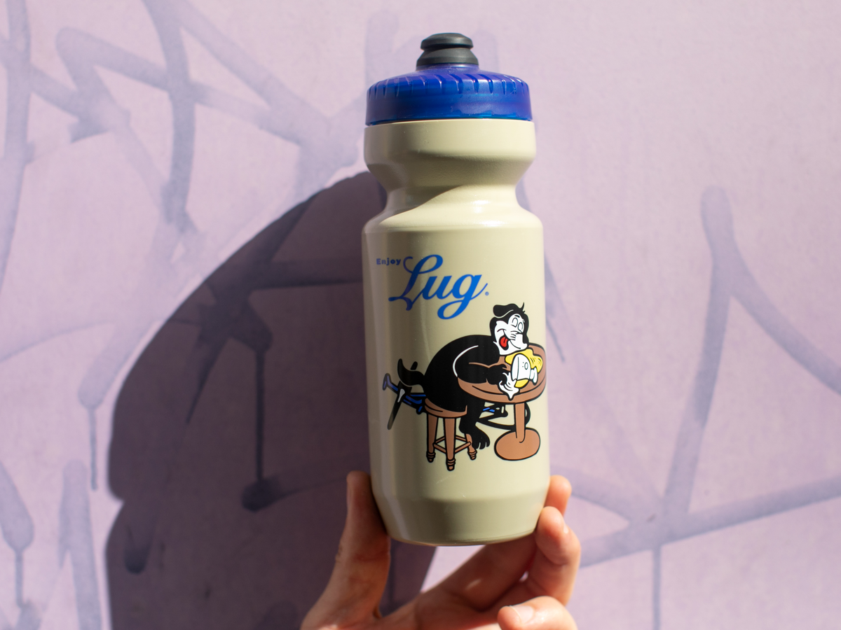 Blue Lug Dog Water Bottle in Mocha with blue cap — "Enjoy Lug." lettering and illustration of the Dog mascot eating at a bar counter