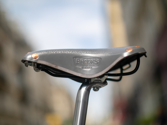 Brooks x Rivendell B17 saddle in gray — side view on a silver seatpost, showing the pebble leather top, copper rivets at the nose, carved lower flap and "Brooks Champion Special B17" embossed stamp