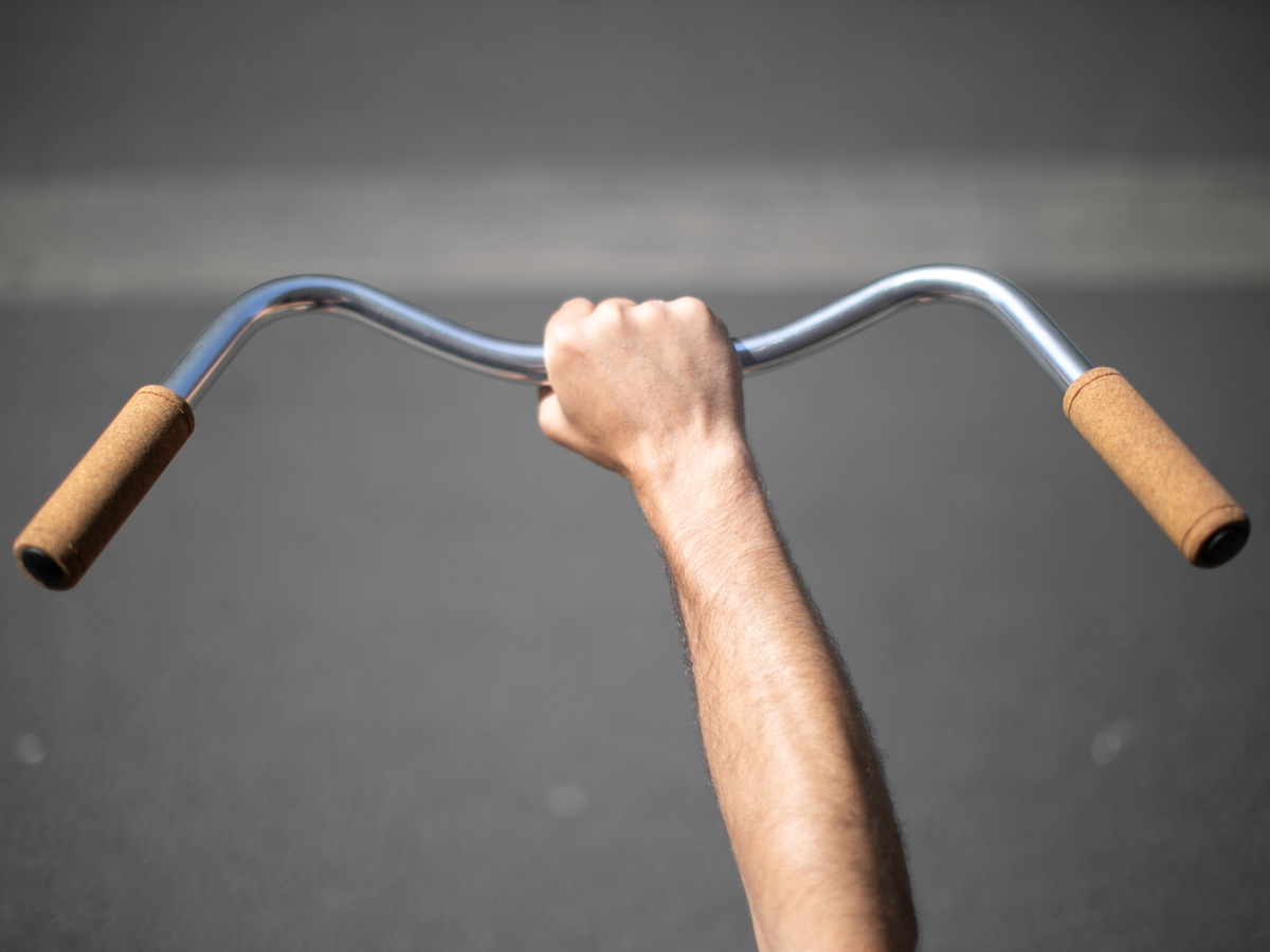 La Mad 1919 Cork Grips installed on a silver swept-back handlebar — both grips visible, held up by a hand against a road background