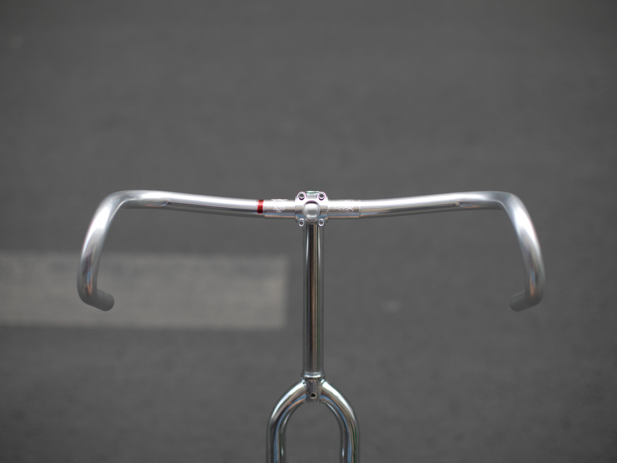 CRUMB x NITTO Futen Drop handlebar front view, polished silver, showing wide flared drop profile and red clamp accent on a chrome stem and fork
