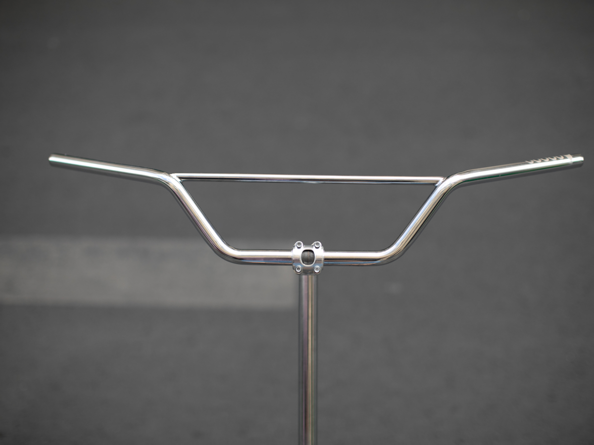 Magic Components Noppo Bar, front view. Chrome CrMo steel handlebar with prominent rise and crossbar brace, shown mounted on a display stand against a grey background.