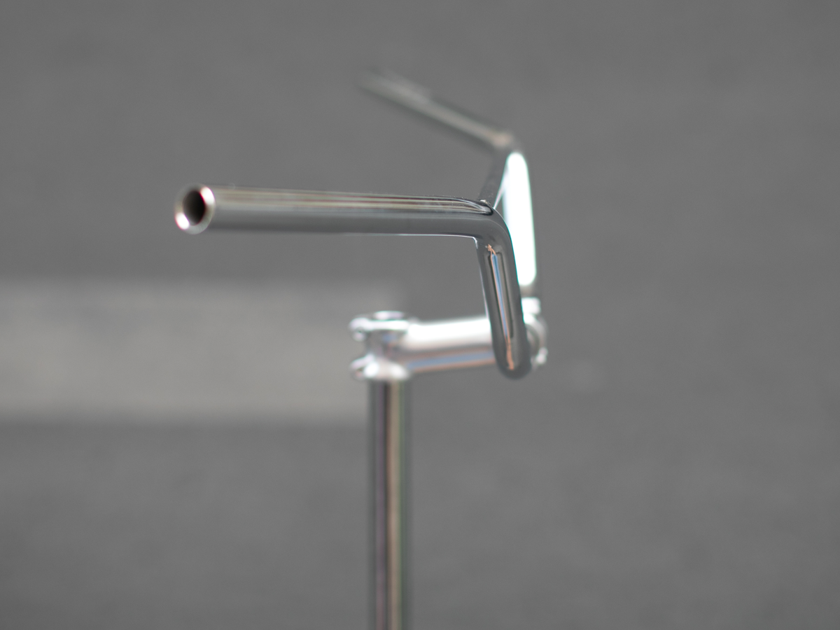 Close-up side view of the Magic Components Noppo Bar showing the upsweep angle at the grip end and the stem clamp junction, highlighting the bar's geometry and chrome finish.