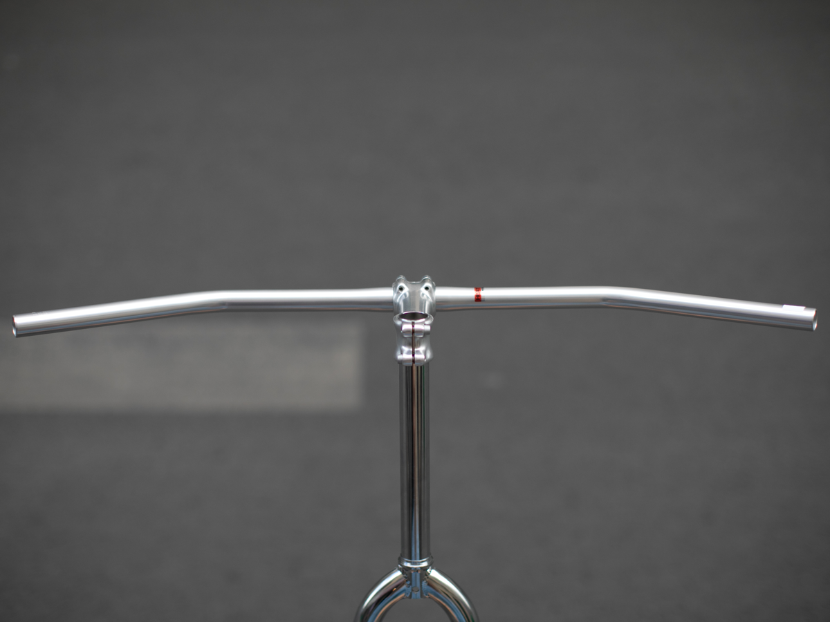Carter Bar in raw aluminum, front view mounted on a quill stem and display stand. The wide, clean silhouette and gentle sweep of the bar are clearly visible.