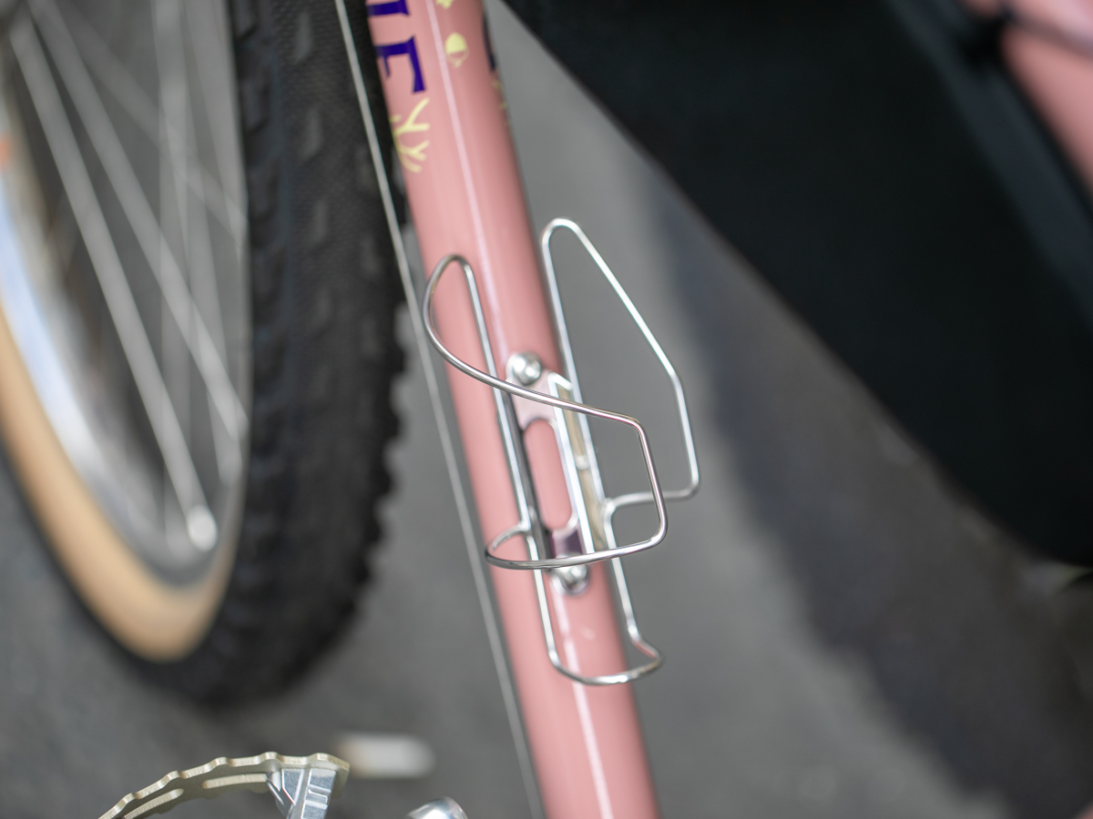 Velo Orange Crescent sideloading bottle cage mounted on a pink bike downtube, shown without a bottle