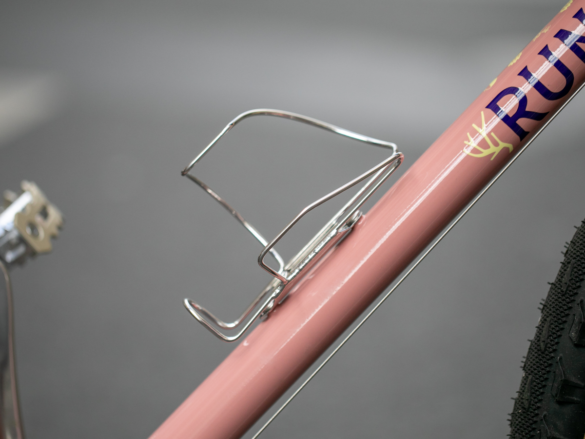 Velo Orange Crescent sideloading bottle cage mounted on a pink bike seattube, empty cage detail view