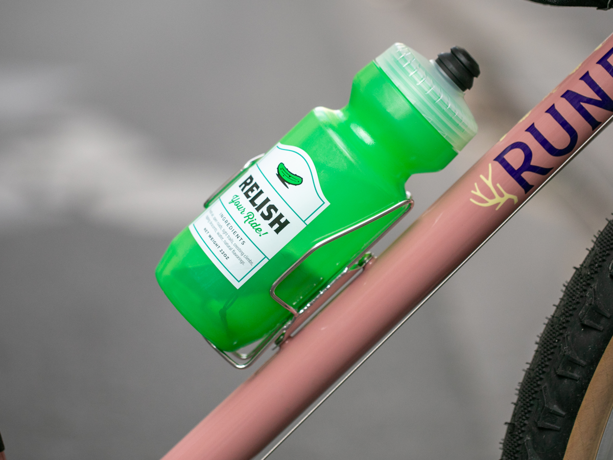 Green water bottle secured in a Velo Orange Crescent sideloading bottle cage on a pink bike