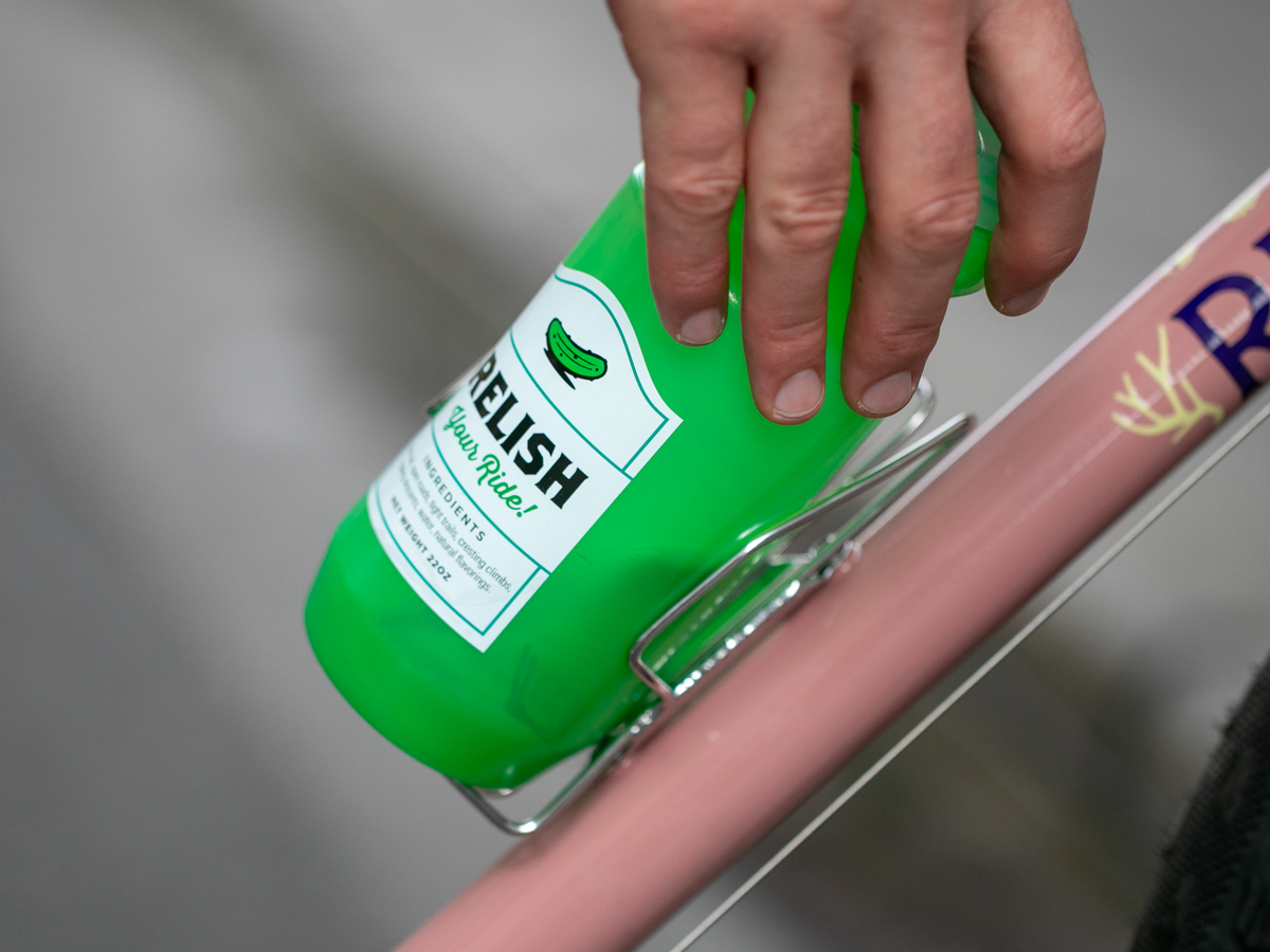 Hand sliding a water bottle sideways into a Velo Orange Crescent bottle cage mounted on a pink bike frame